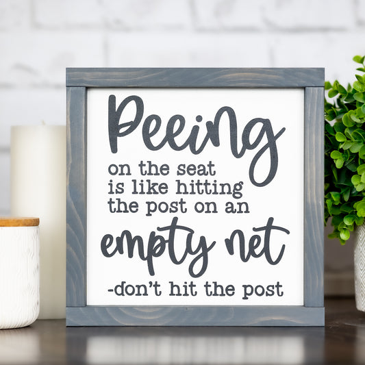 peeing on the seat is like hitting the post on an empty net ~ wood sign